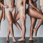 Five women wearing grey underwear are pictured from the abdomen down with smooth legs pose together
