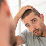 Young man looking at hair in mirror after hair transplant