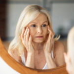 Woman looking in the mirror at eyelids considering blepharoplasty surgery