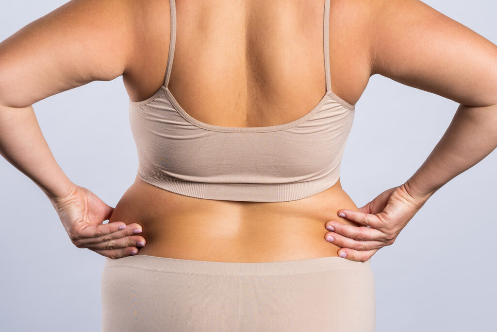 Woman's back, hips, and buttocks, with her hands squeezing fat on flanks (love handles)
